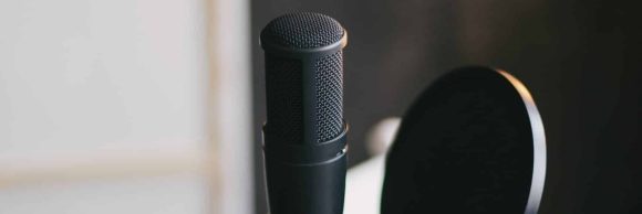 Items for recording podcast: professional microphone, earphones and laptop on white table in cozy home studio with black walls and lots of plants.